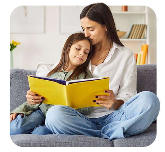 Mujer adulta junto a su hija leyendo un libro en un sofá 