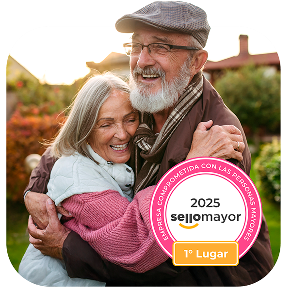 Fotografía de una pareja de adultos mayores abrazados y sonriendo, con el distintivo circular rosa de Sello Mayor 2025 que los acredita en el Primer Lugar como Empresa Comprometida